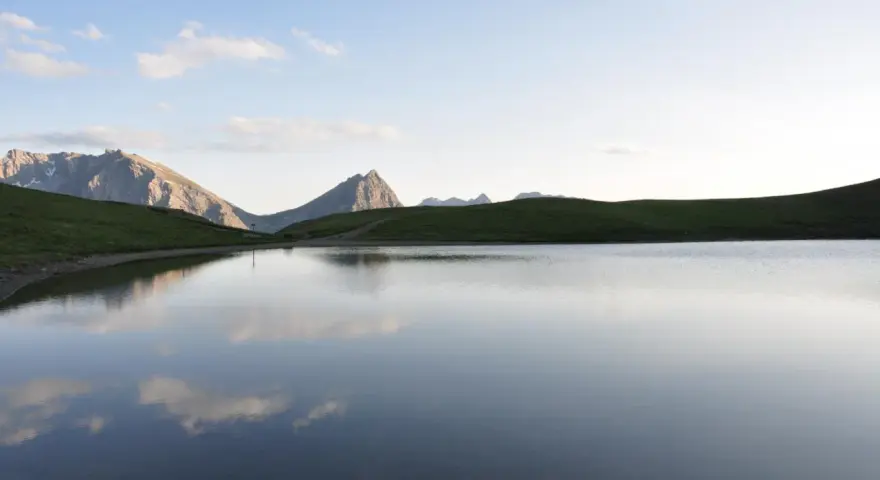 Sestriere estate: un lago alpino riflette le montagne e il cielo azzurro, un'oasi di pace.