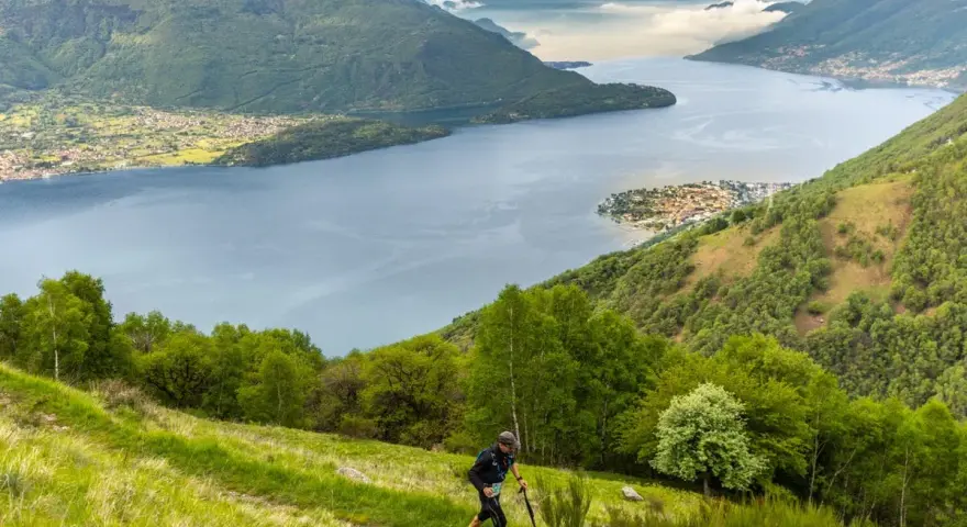 Un atleta corre su un sentiero erboso con vista sul Lago di Como, un'emozionante randonnée.