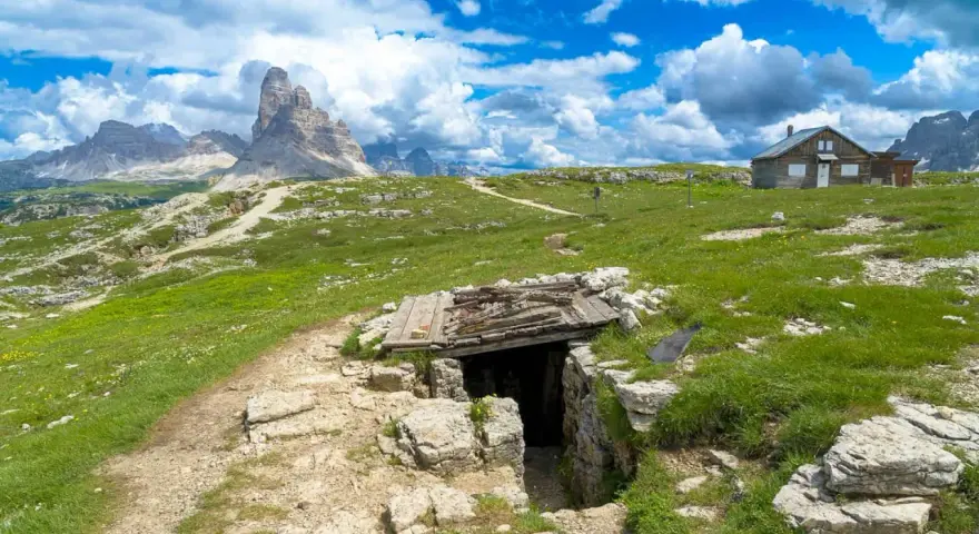 Un sentiero conduce a un rifugio di guerra sul Monte Piana, con le maestose Tre Cime di Lavaredo sullo sfondo.
