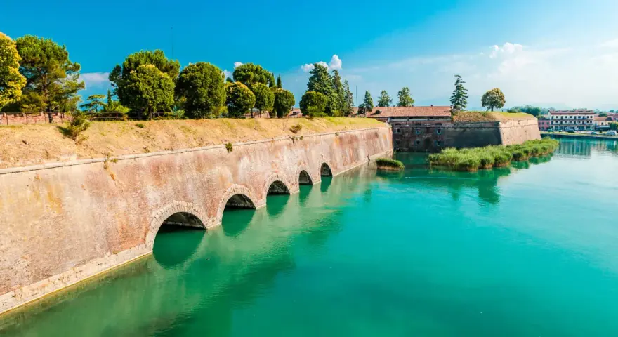 Fortificazioni storiche con archi in mattoni e acqua turchese, dove si trova Peschiera del Garda.