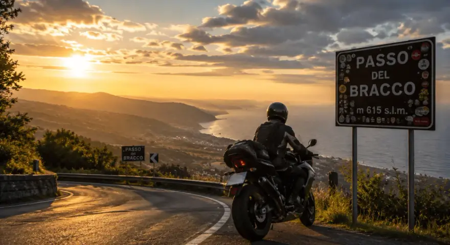 Motociclista al Passo del Bracco al tramonto, con vista sul mare e sulle colline illuminate dalla luce dorata.