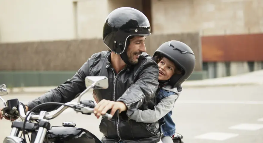 Padre e figlio sorridono in moto, rispettando il nuovo codice della strada per bambini in moto.