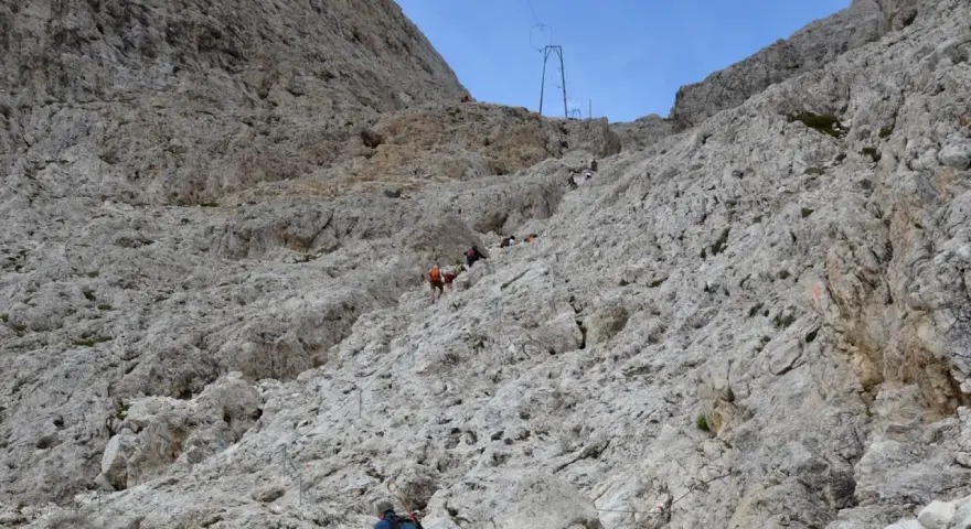Escursionisti affrontano la **difficoltà** del sentiero verso il **Rifugio Re Alberto**, aggrappandosi a cavi d'acciaio su un ripido pendio roccioso.
