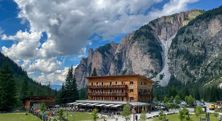 Edificio in legno a Pederu San Vigilio, con montagne imponenti e cielo nuvoloso.