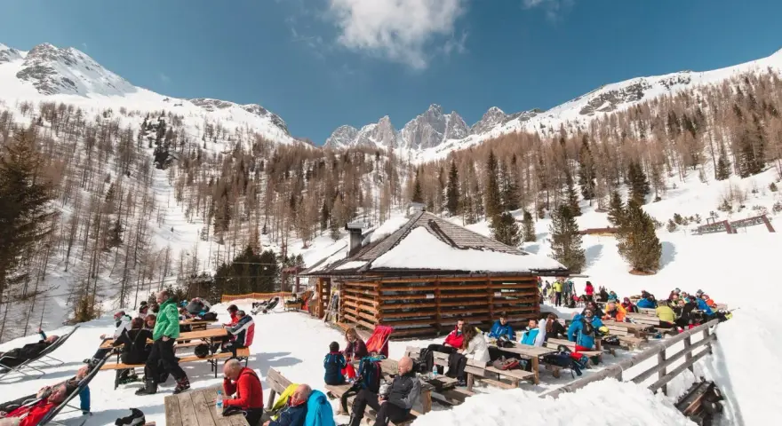 Malga Valcigolera, un rifugio alpino innevato con gente seduta ai tavoli. Per sapere come arrivare, guarda l'immagine.