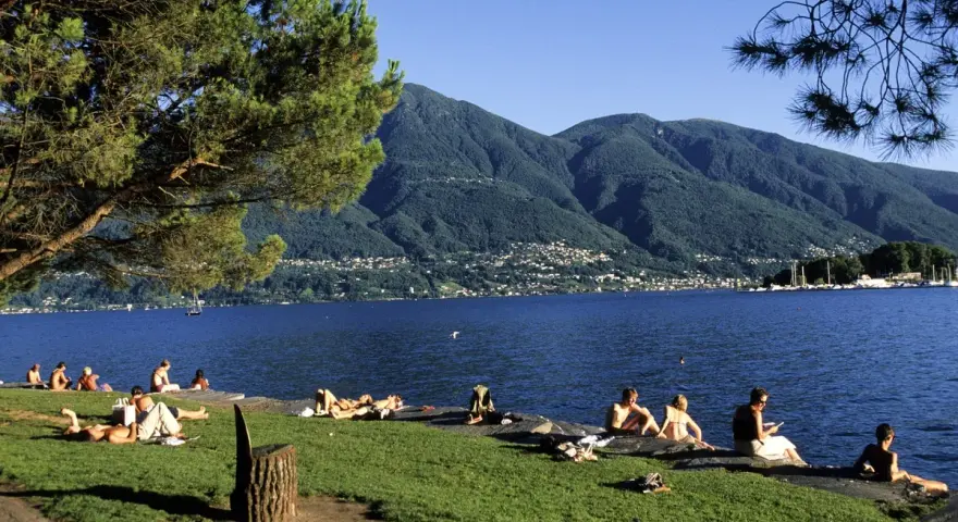 Persone rilassate sui prati e sulle rive di uno dei bellissimi laghi piemontesi, con montagne verdi sullo sfondo.
