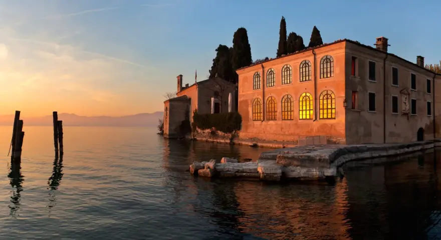 Punta San Vigilio: un tramonto dorato illumina la spiaggia e l'antica villa affacciata sul lago.