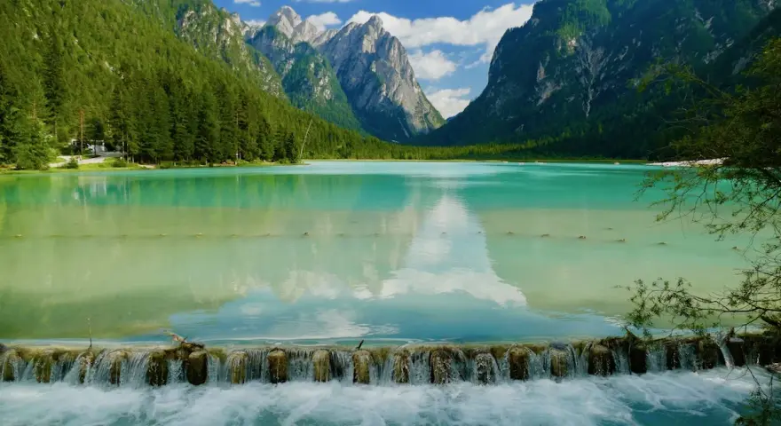 Splendido lago turchese incastonato tra montagne verdi, ideale per una toblacher see wanderung. Una cascata artificiale crea un effetto scenografico.
