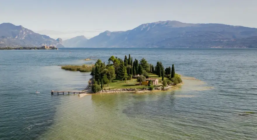 Un'incantevole isola dei conigli sul Lago di Garda, con un piccolo molo e una casetta gialla tra i cipressi.