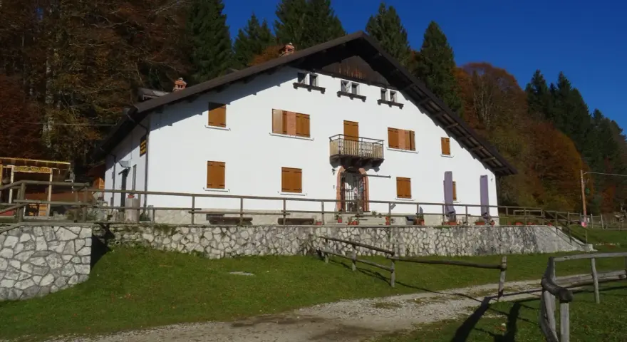 Il rifugio Città di Vittorio Veneto, immerso nel foliage autunnale, accoglie con la sua facciata bianca e le finestre con persiane in legno.