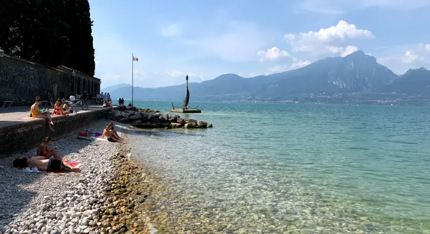 Persone rilassate sulla torri del benaco spiaggia, con acque limpide e montagne sullo sfondo.