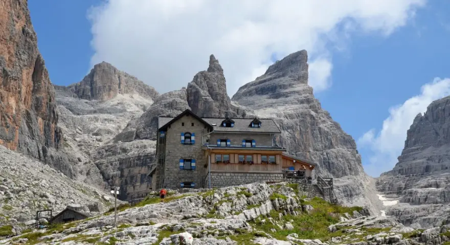Il rifugio Tuckett e Sella, un'oasi di pietra tra le imponenti vette dolomitiche, accoglie escursionisti sotto un cielo azzurro e nuvoloso.