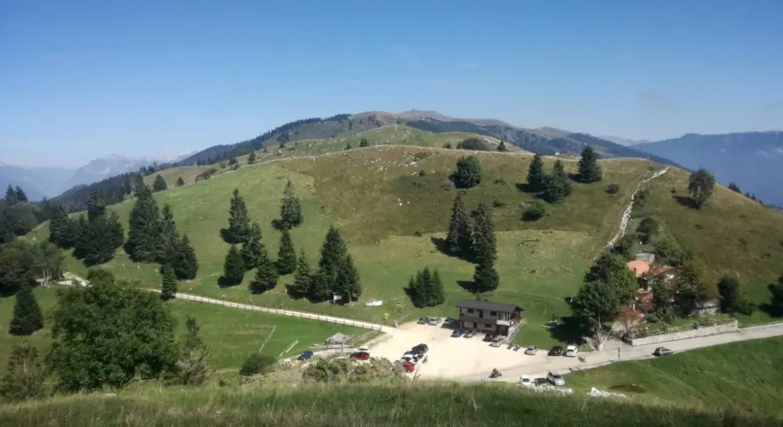 Panorami verdi e dolci colline del Pian delle Femene, con un rifugio e parcheggio.