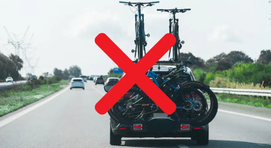 Attenzione al carico sporgente auto! Biciclette sul portabici posteriore, ma una grande X rossa indica un problema di sicurezza.