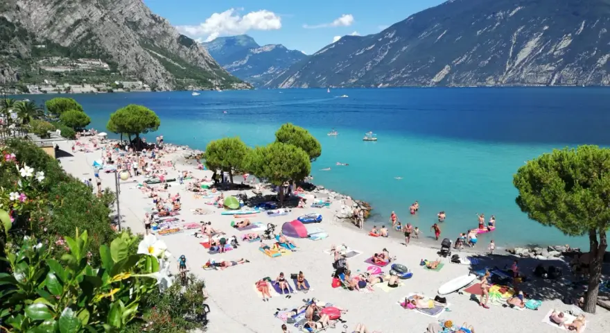 Una vivace spiaggia di Limone sul Garda, con gente che prende il sole e nuota nelle acque turchesi del lago.