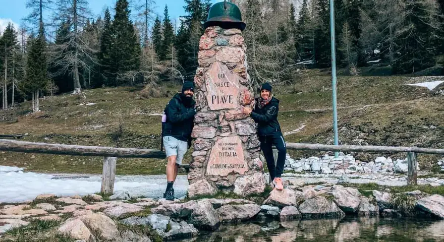 Coppia sorridente vicino a un monumento in pietra a Sappada, ideale per passeggiate facili.