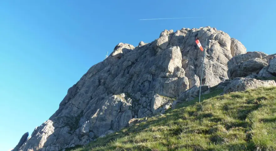 Vetta rocciosa con bandiera segnavento. Per col rodella come arrivare, segui il sentiero erboso verso la cima.
