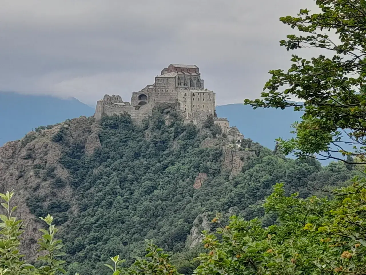 Abbazia di San Michele della Chiusa, un imponente complesso monastico arroccato su un colle roccioso, circondato da una fitta vegetazione.