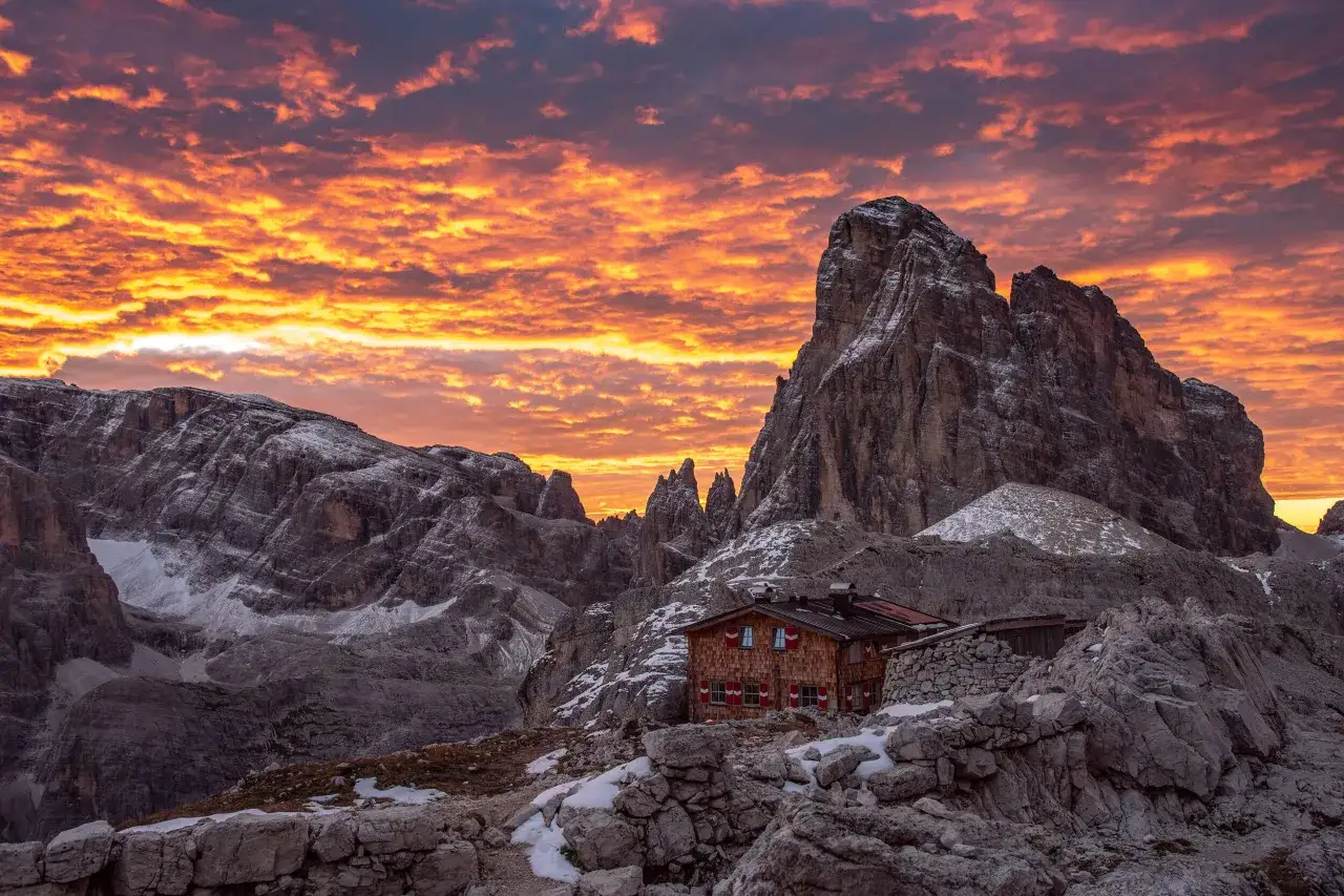 Al tramonto infuocato, il rifugio Pian di Cengia si staglia tra le rocce innevate, un nido accogliente nel cuore delle Dolomiti.