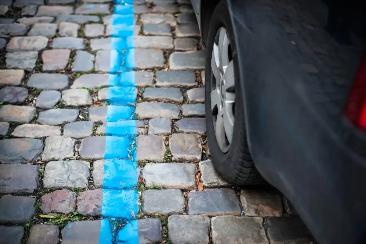 Ruota di un'auto su un selciato con striscia blu. Ricorda che nei giorni festivi si paga il parcheggio.