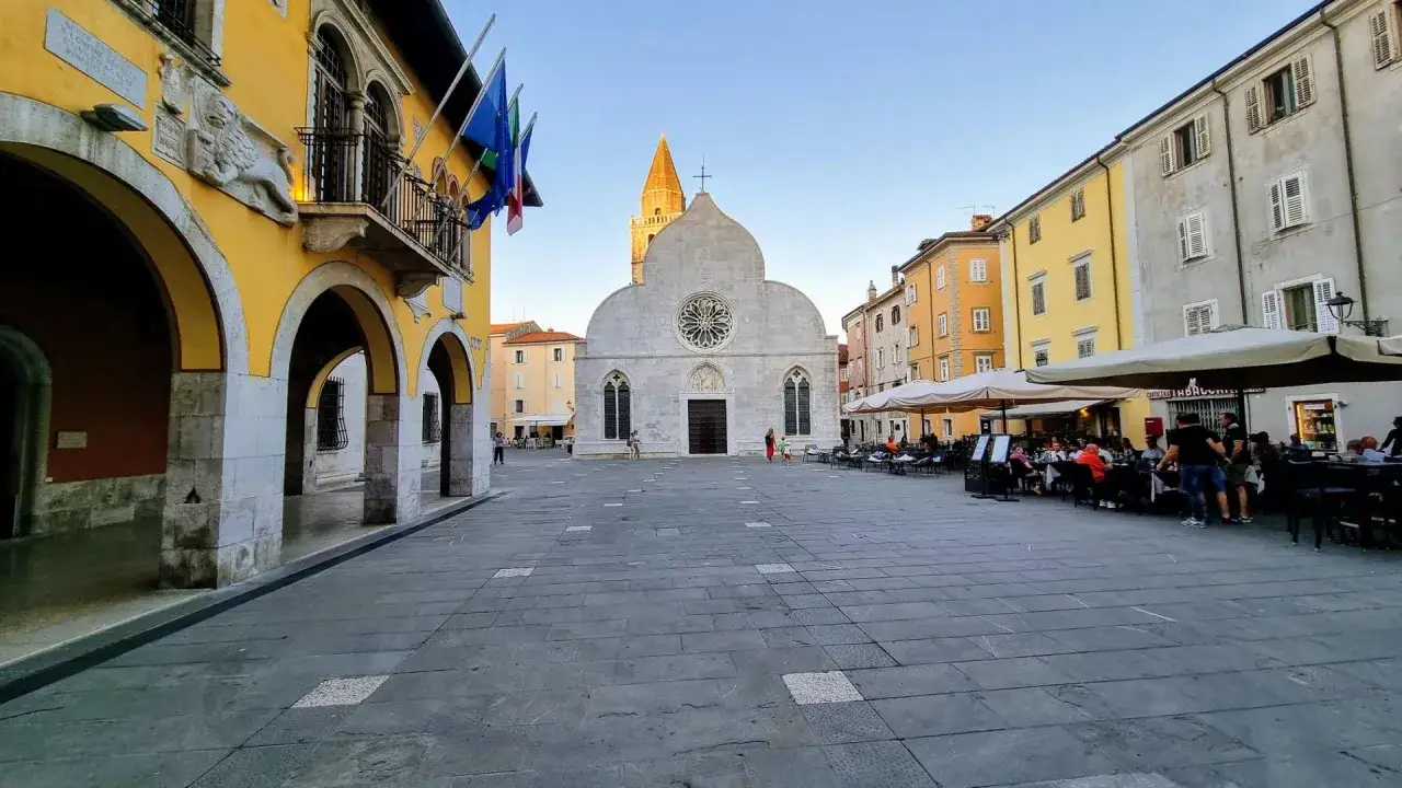 Piazza di Muggia con la cattedrale, edifici colorati e tavolini all'aperto. Cosa vedere in questa splendida cornice.