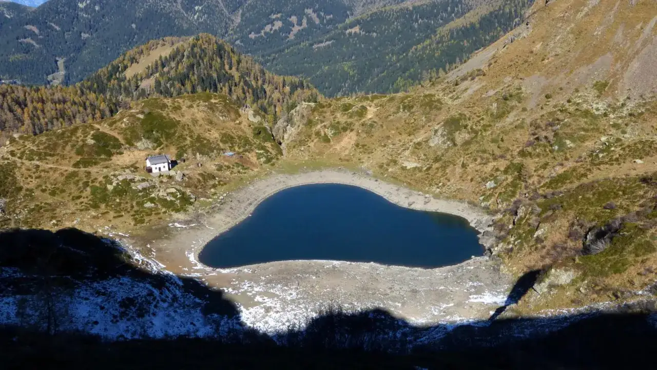 Il lago di Erdemolo, con la sua forma a cuore, riflette il cielo tra montagne brulle e un piccolo rifugio.