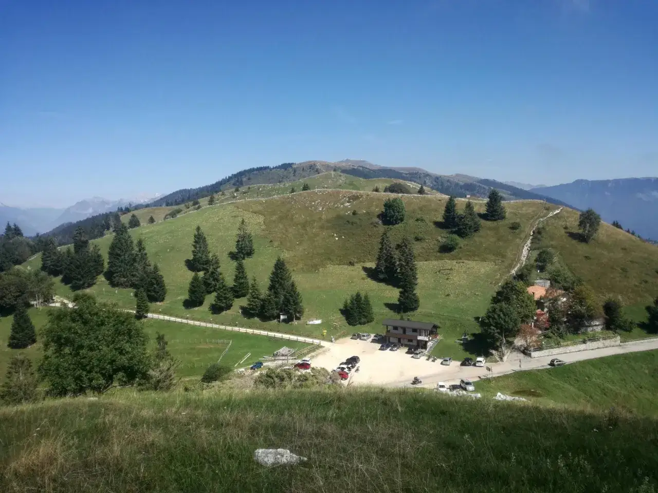 Panorami verdi e dolci colline sul Pian delle Femene, con un rifugio e parcheggio.