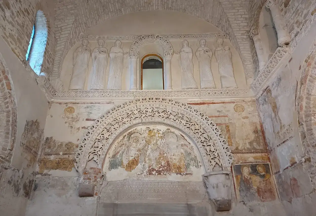 Interno di Cividale del Friuli: affreschi e rilievi antichi narrano storie sacre sotto un arco decorato.