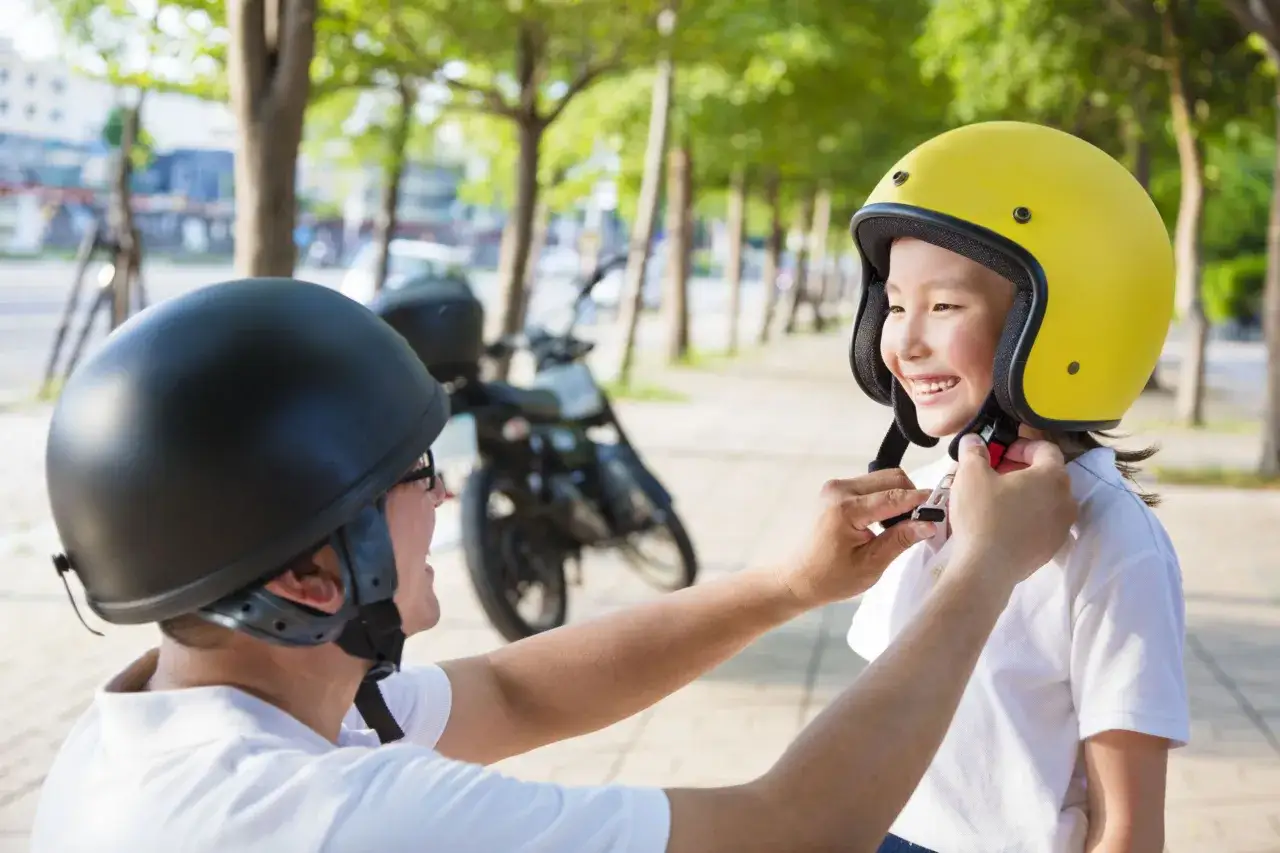 Un adulto aiuta un bambino a indossare il casco giallo, pronto per un giro in moto nel rispetto del nuovo codice della strada.