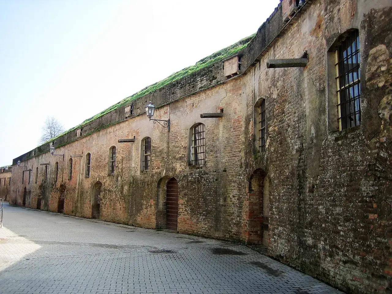 Mura storiche di Pizzighettone, cosa vedere: un lungo muro di mattoni con finestre ad arco e lampioni, che invita a scoprire la storia del luogo.