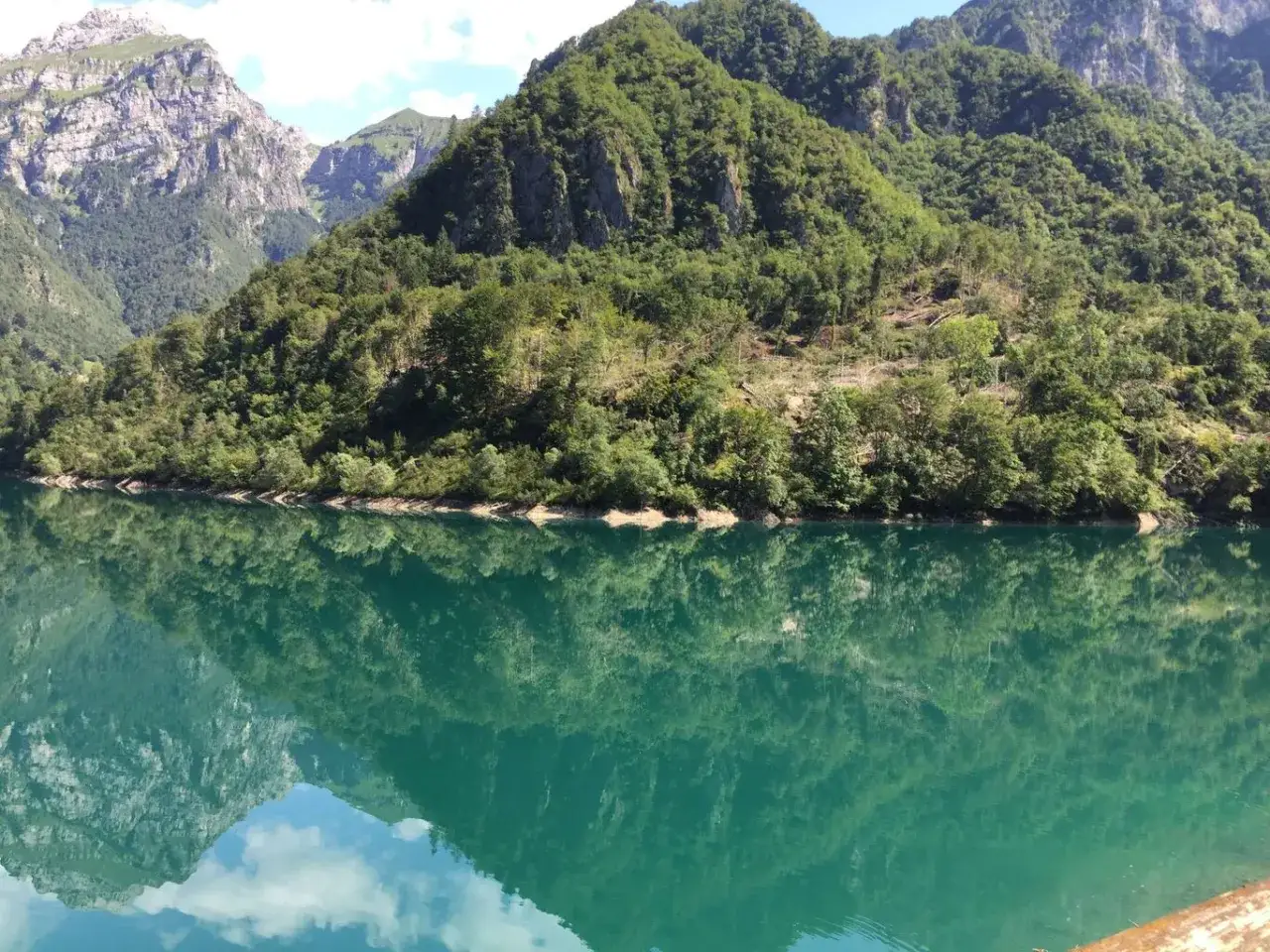 Il lago della Stua riflette montagne verdi e cime rocciose, creando uno specchio d'acqua cristallina.