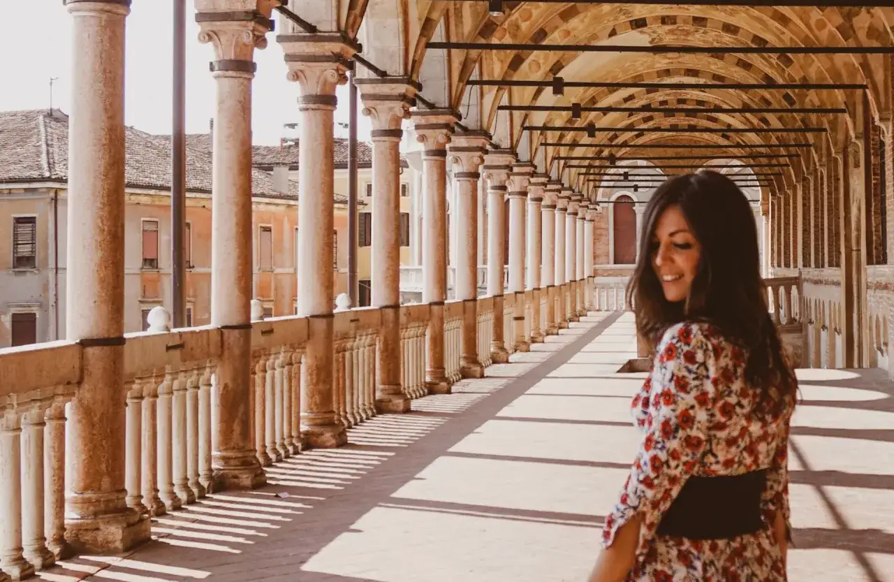 Una donna sorride mentre passeggia sotto un portico con colonne, un'istantanea perfetta per scoprire Padova in un giorno.