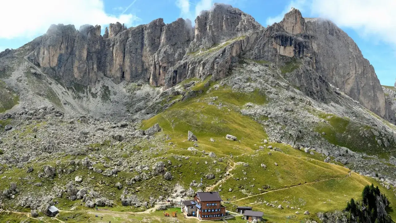Sentiero panoramico per il giro del Catinaccio, con rifugio alpino e imponenti pareti rocciose.