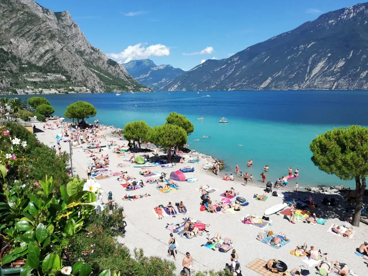 Spiaggia affollata a Limone sul Garda, bagnanti prendono il sole e si rinfrescano nelle acque turchesi del lago.