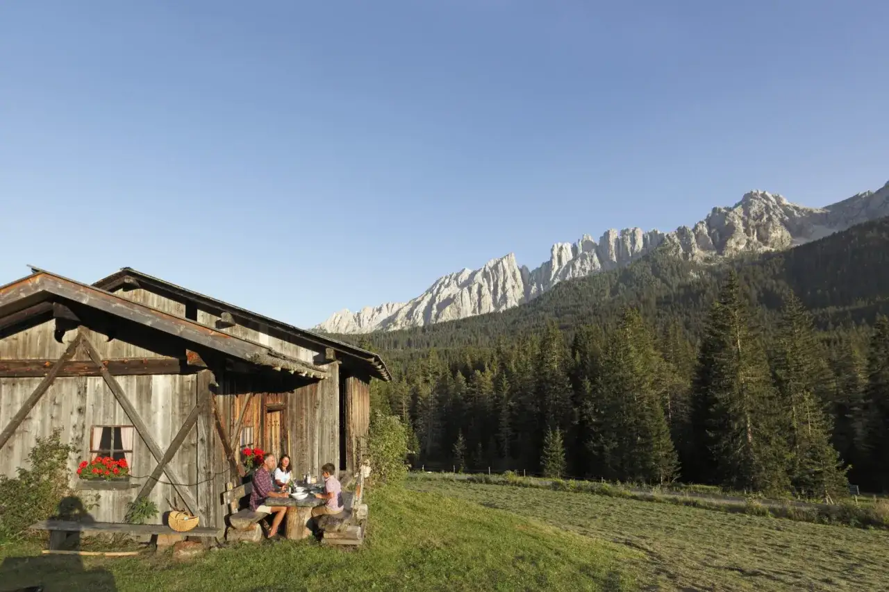 Una famiglia pranza all'aperto davanti alla malga Molvine Binot, con le maestose vette delle Dolomiti sullo sfondo.
