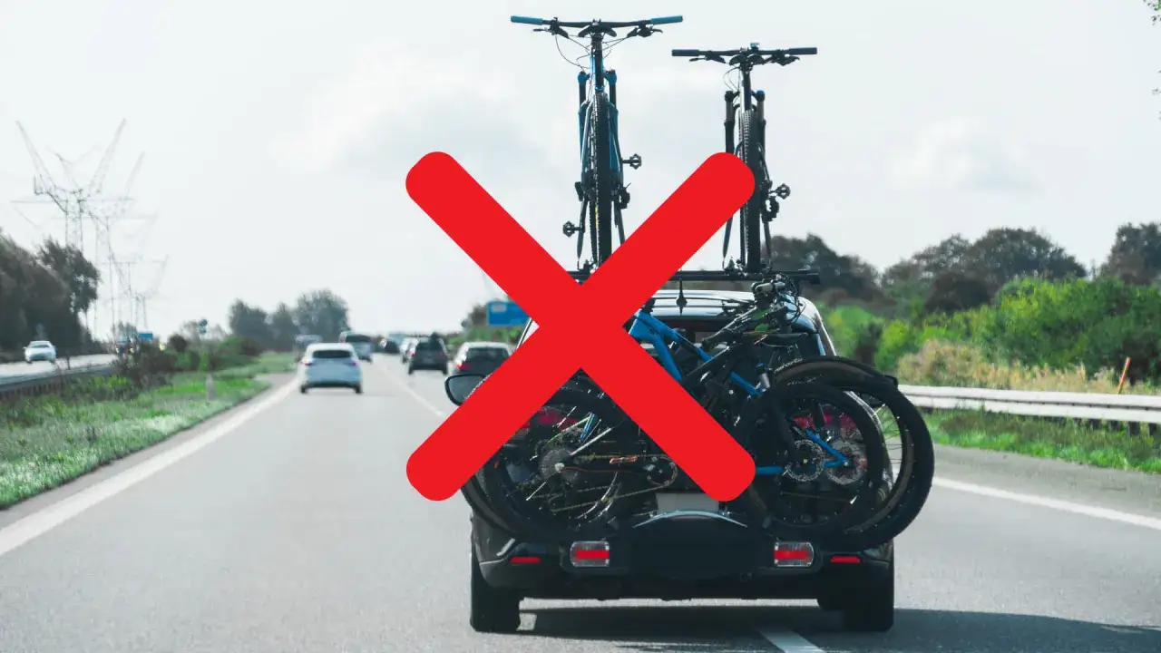 Carico sporgente auto con biciclette sul portapacchi posteriore, segnalato da una grande croce rossa.