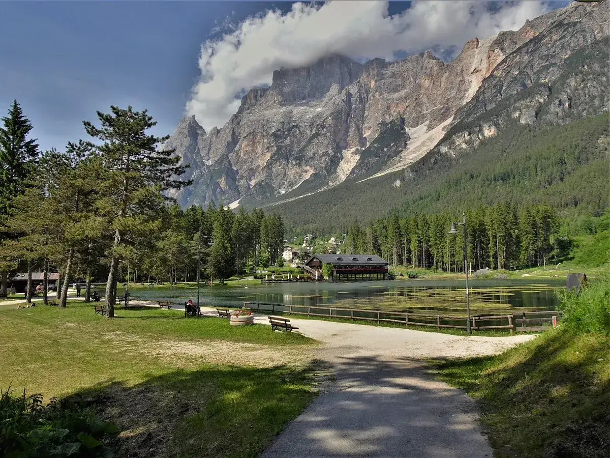 Passeggiata serena al lago di San Vito, con imponenti montagne sullo sfondo e un bosco di conifere che abbraccia le rive.