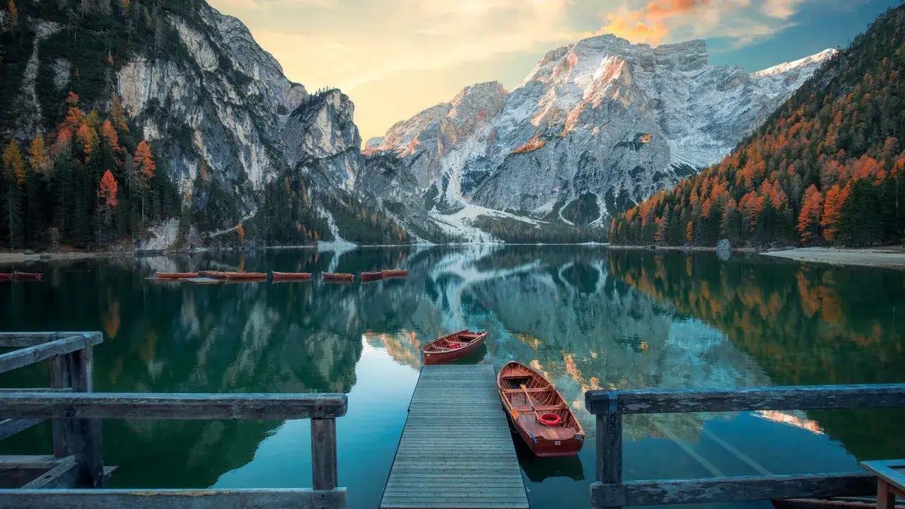 Barche di legno sul lago calmo del Pragser Wildsee, con montagne maestose e boschi autunnali che si specchiano nell'acqua cristallina.