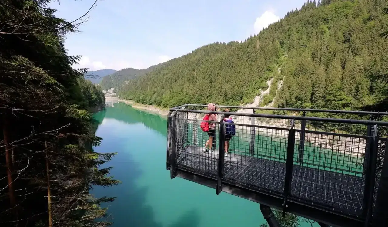 Due persone su una piattaforma panoramica ammirano il lago di Val Noana. Ecco come arrivare a questo splendido specchio d'acqua alpino.