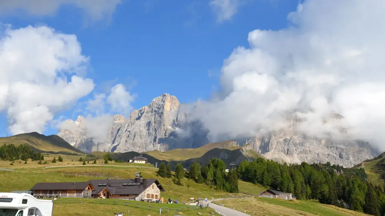 Panorami mozzafiato al Passo Rolle: malghe, boschi e vette imponenti sotto un cielo azzurro con nuvole bianche. Cosa vedere in questo paradiso alpino.