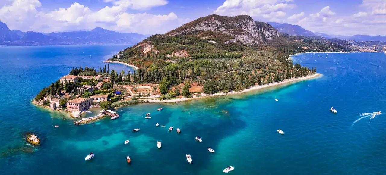 Punta San Vigilio: incantevole spiaggia con ville storiche, uliveti e barche che solcano le acque cristalline del lago.