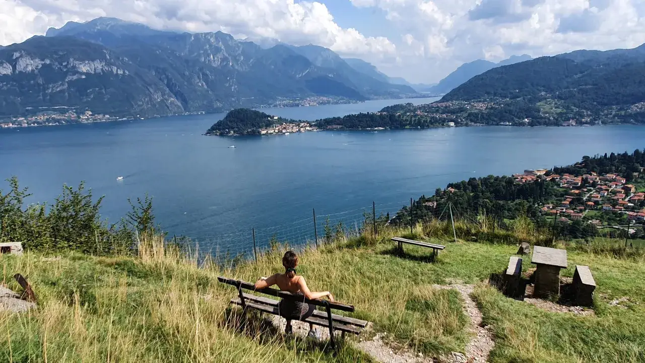 Vista panoramica mozzafiato durante una randonn&eacute;e sul Lago di Como. Una persona seduta su una panchina ammira il paesaggio.