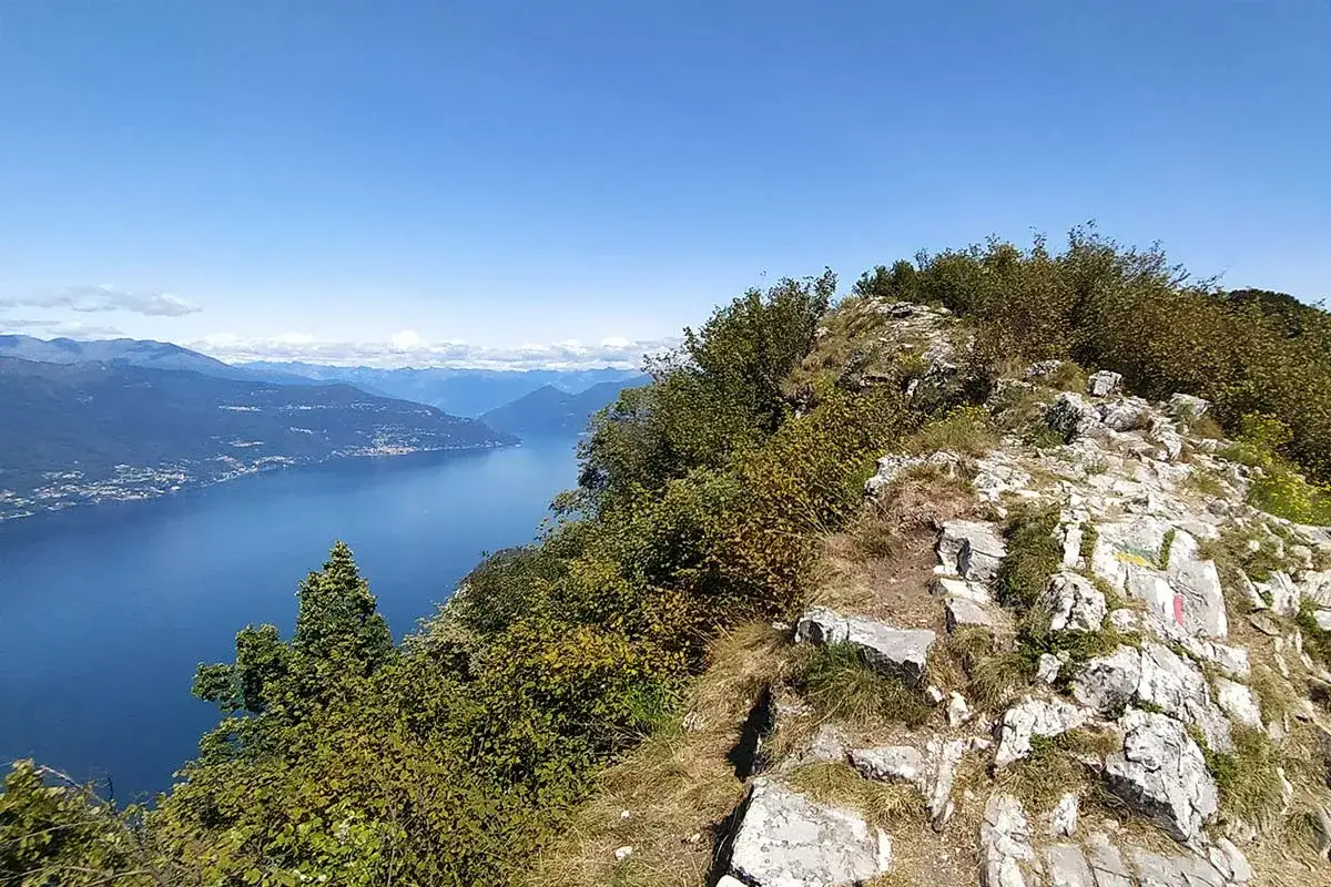 Sentiero roccioso sui Pizzoni di Laveno, con vista sul lago e montagne.