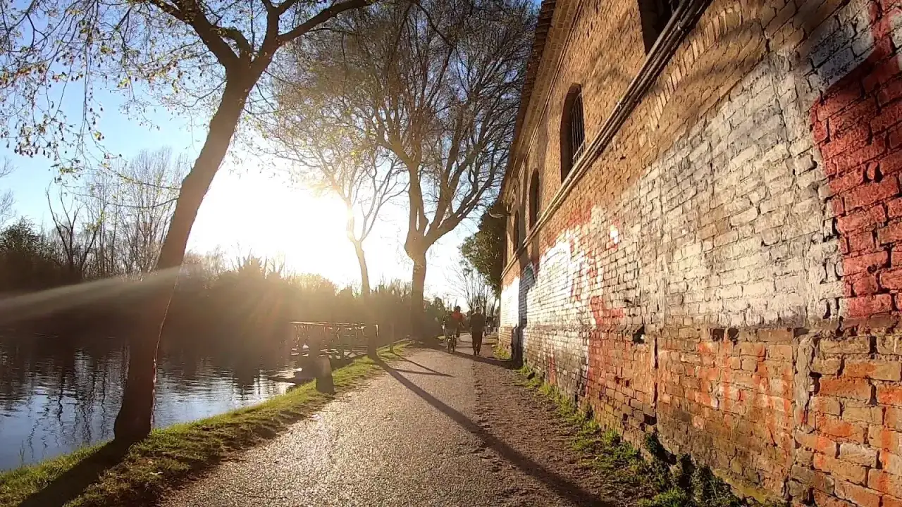 Passeggiata lungo il fiume a Casale sul Sile, con un antico muro di mattoni e alberi spogli illuminati dal sole del tramonto.