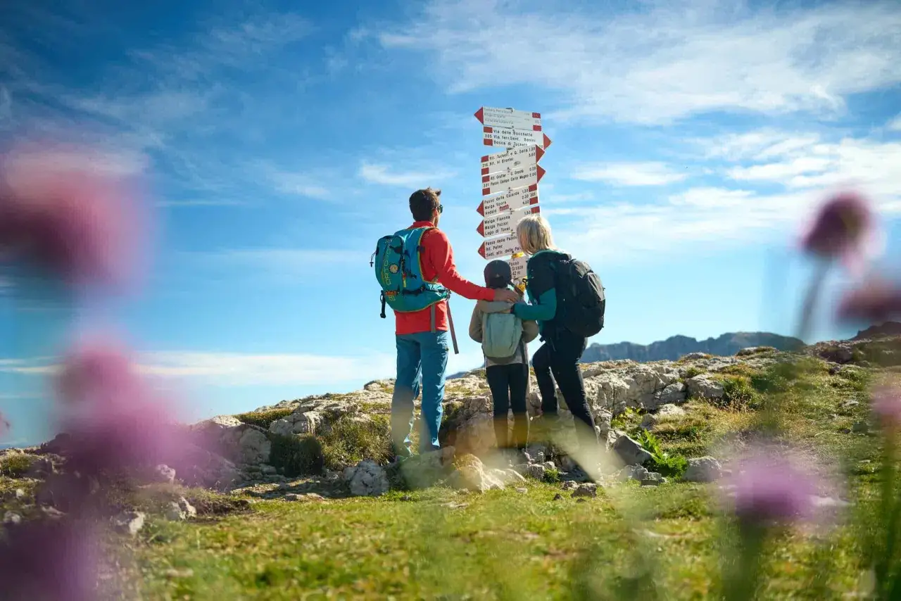 Famiglia in cima a una montagna in Trentino, con cartelli che indicano sentieri per un facile trekking.