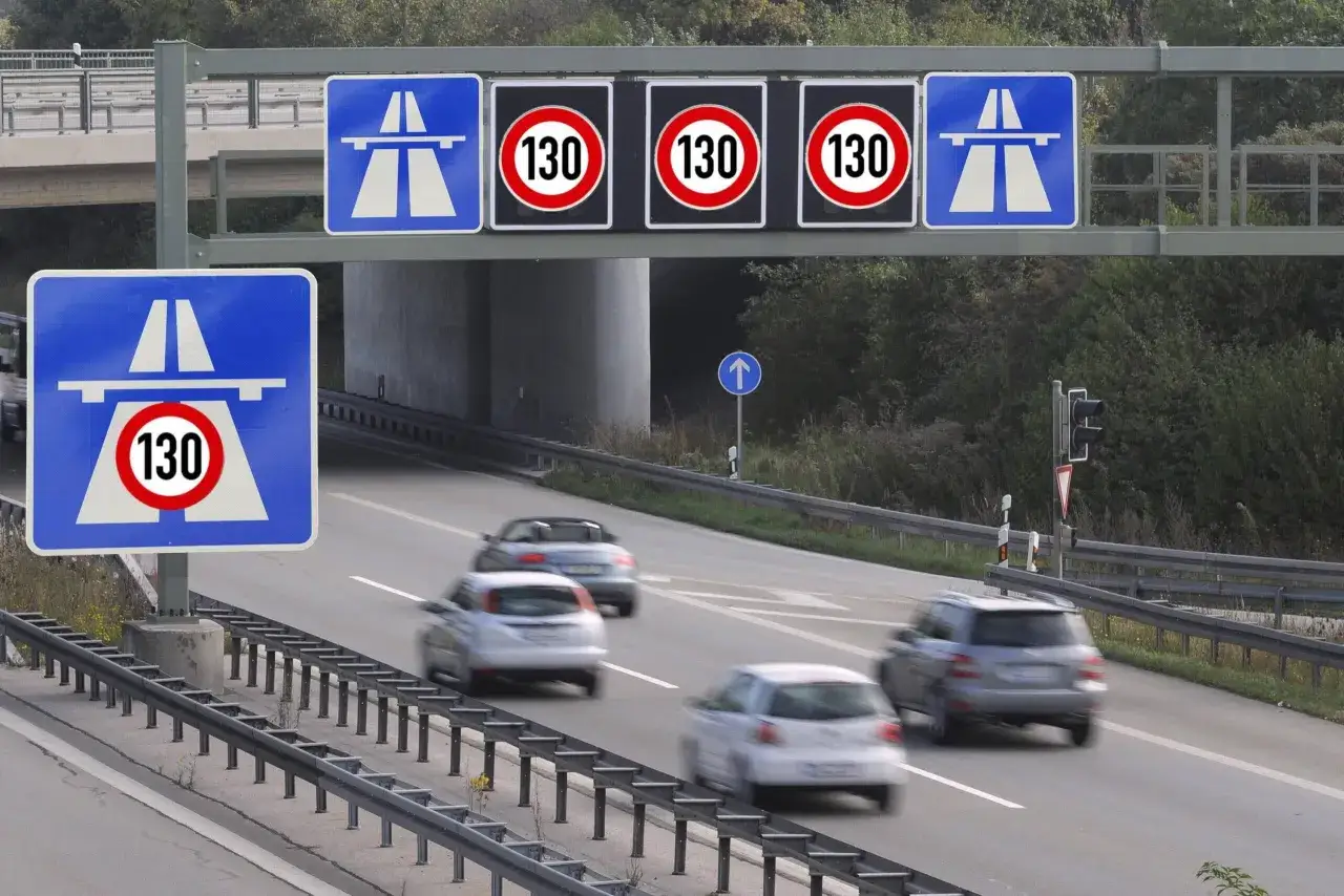 Segnali di limite velocit&agrave; autostrada 130. Auto in transito su strada a pi&ugrave; corsie, con cartelli blu che indicano l'autostrada e segnali circolari rossi con il numero 130.