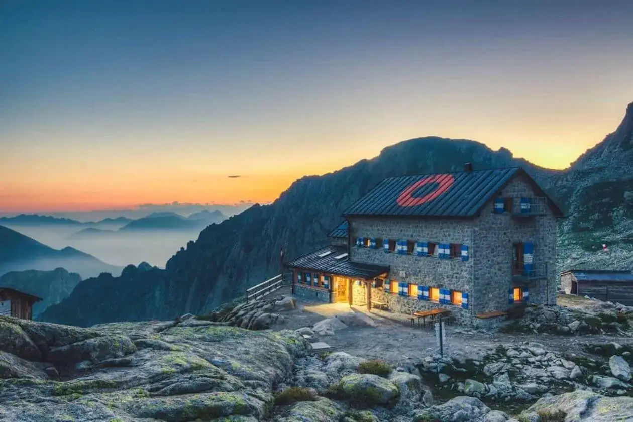 Rifugio Cima d'Asta illuminato al tramonto, con montagne nebbiose all'orizzonte.