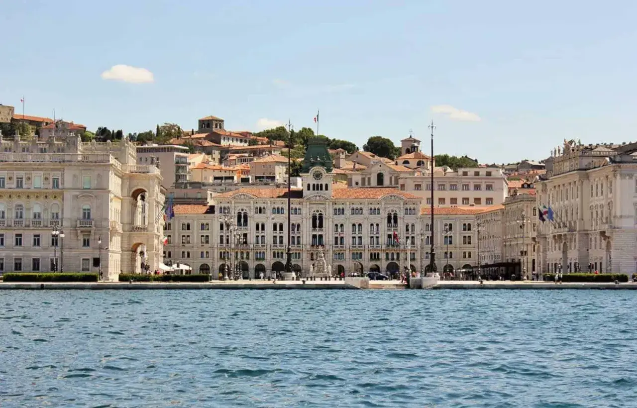Piazza Unit&agrave; d'Italia, un gioiello da vedere a Trieste, si affaccia sul mare con palazzi imponenti e un cielo azzurro.