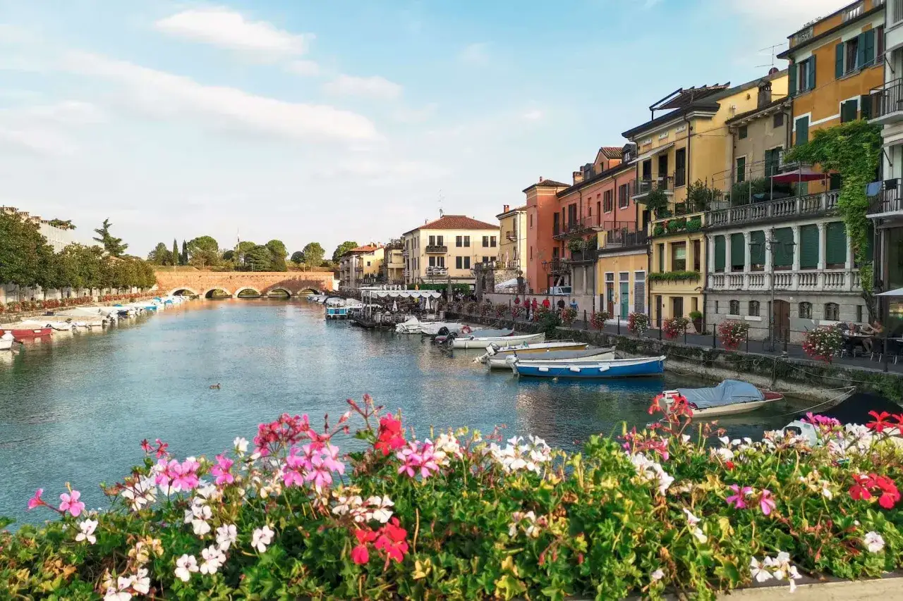Un canale sereno con barche ormeggiate e case colorate, un'atmosfera da cartolina che ricorda i paesi vicino Peschiera del Garda.