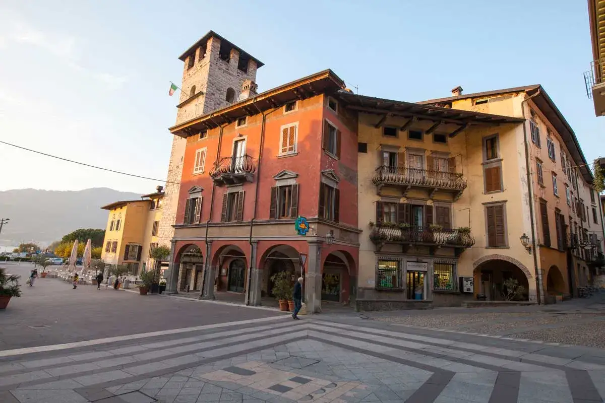 Piazza a Pisogne, cosa vedere: un borgo con torre medievale, palazzi colorati con portici e balconi fioriti, ideale per una passeggiata.